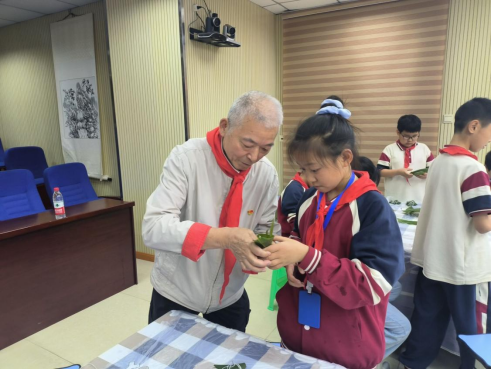 50年党龄老党员教学生包粽子。两路街道办事处供图 华龙网发