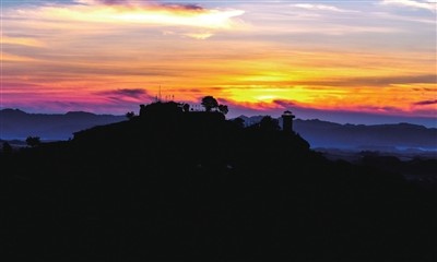 In the Huashi Ancient Village scenic spot, the crimson sunset sets the rolling mountains and the ancient village aglow, forming a stunning silhouette against the vividly hued sky