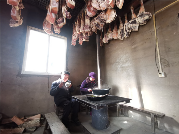 李光福和妻子正在火炉旁吃饭，一块块猪肉挂满了整个房间。华龙网-新重庆客户端 冉长军 摄