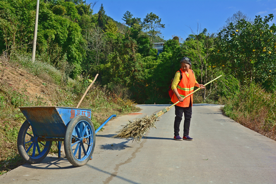 复平镇小山社区九组的乡村道路上，贫困户蒋德珍正打扫清洁。特约通讯员 张常伟 摄