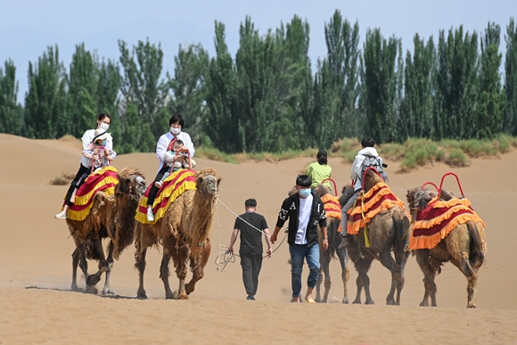 游客在新疆鄯善县库木塔格沙漠风景区骑骆驼游览。