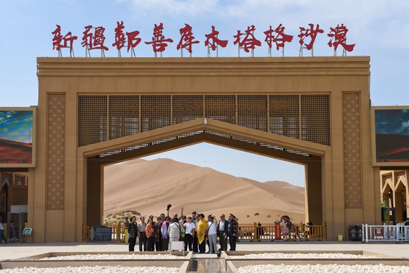 游客在新疆鄯善县库木塔格沙漠风景区门口拍照留念。