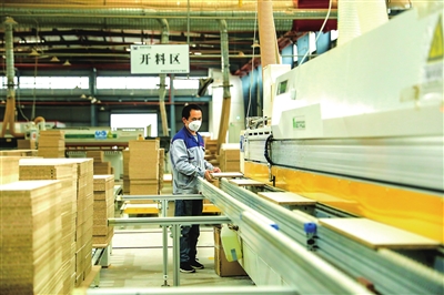 重庆天荣家居有限公司生产车间，工人在对板材进行自动封边作业。