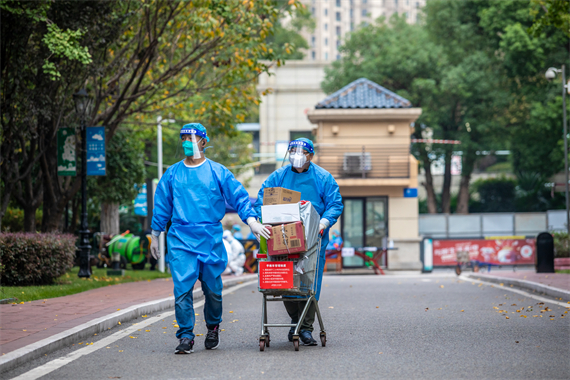 永川职教中心党委委员、副校长鄢泽彬（推车者）为所在小区居民送生活物资上门