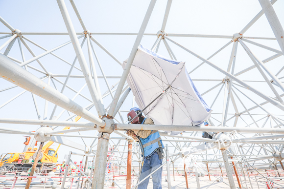 江北国际机场T3B施工现场，电焊工人撑伞在烈日下作业。华龙网-新重庆客户端记者 李裕锟 摄