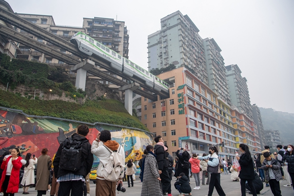 在位于重庆市渝中区的轨道交通李子坝站附近，游客在观看、拍摄“穿楼而过”的列车。