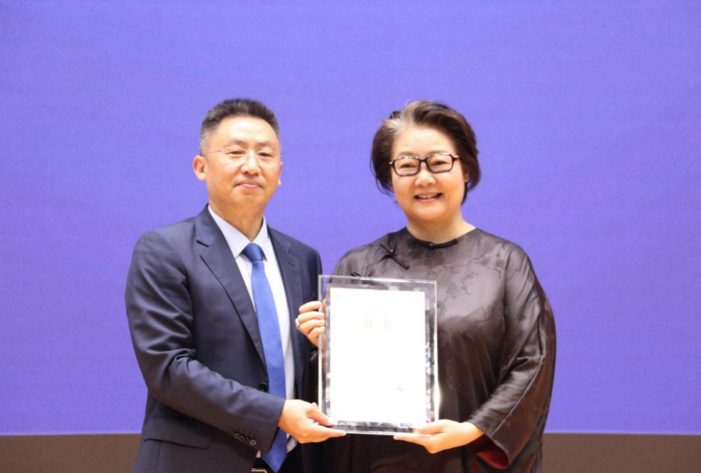 重庆对外经贸学院校长李明海(左)为萨日娜颁发影视融媒体学院院长聘书。受访单位供图