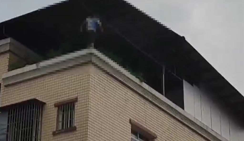 1小伙站在楼顶围墙上，试图轻生。重庆荣昌警方供图