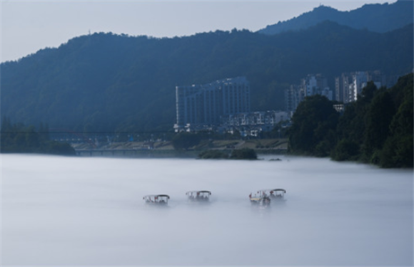 7月16日清晨，游客乘坐“竹筏”造型电动游船，在建德新安江的江雾中前行。新华社记者 徐昱 摄