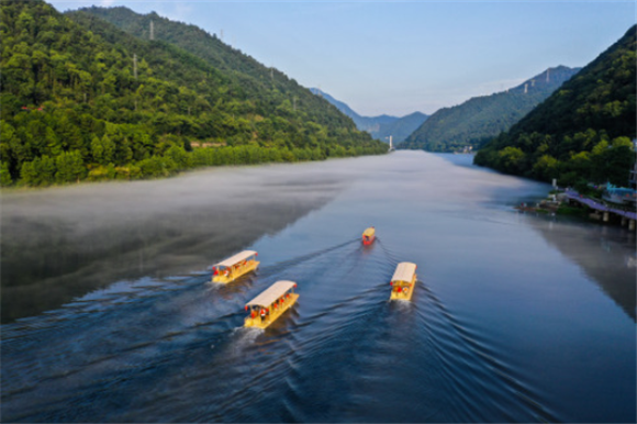 7月16日清晨，游客乘坐“竹筏”造型电动游船，在建德新安江的江雾中前行（无人机照片）。新华社记者 徐昱 摄