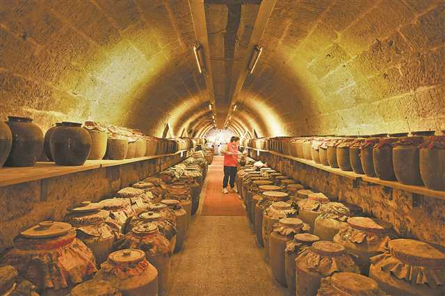 Under the yellow light, workers were holding wine with a vessel at the wine cellar in the air-raid shelter in Shangqingsi Sub-district, Yuzhong District.